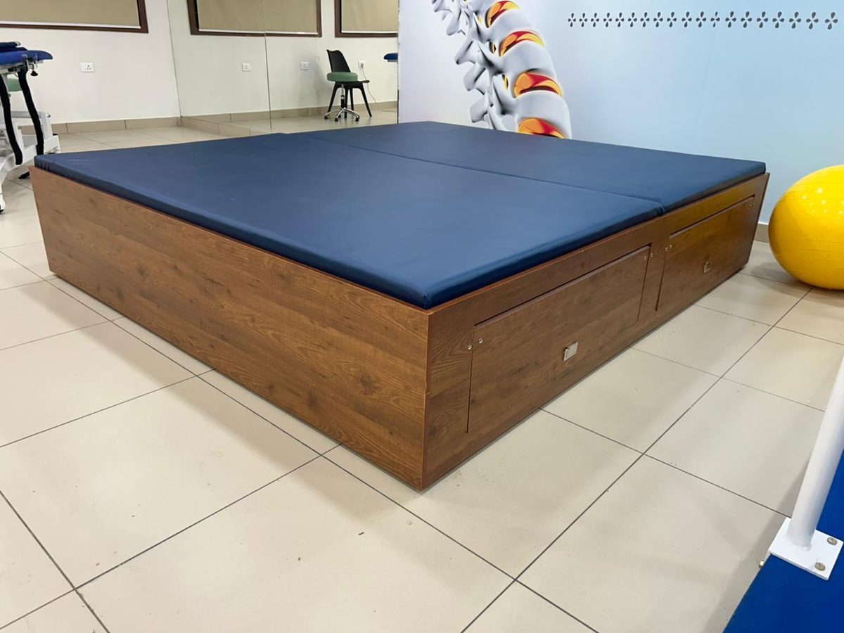 XINIX Bobath table with navy upholstered top and wood-finish base with integrated storage, installed in a rehabilitation facility